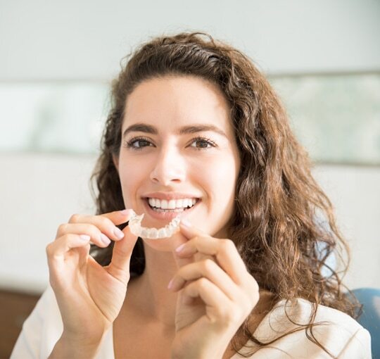 Young woman smiling while inserting an Invisalign clear aligner tray.