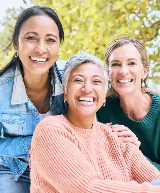Three smiling women posing together outdoors in Bellevue, representing dental practice team and patient care.